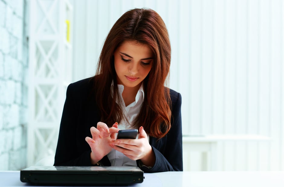 Young serious businesswoman typing on her smartphone in office
